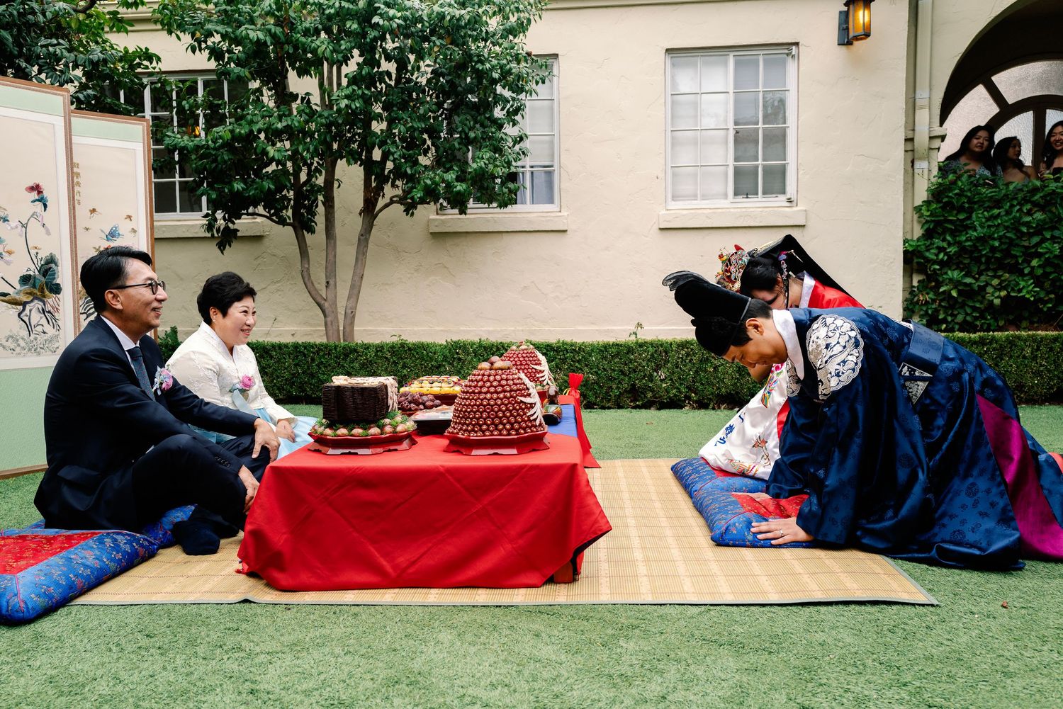 Bride and groom in colorful hanbok performing traditional Korean paebaek bowing ceremony outdoors.