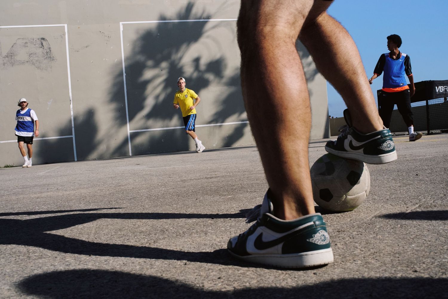 Close-up of a person's foot in Nike Air Jordan sneakers dribbling a soccer ball on an outdoor court.