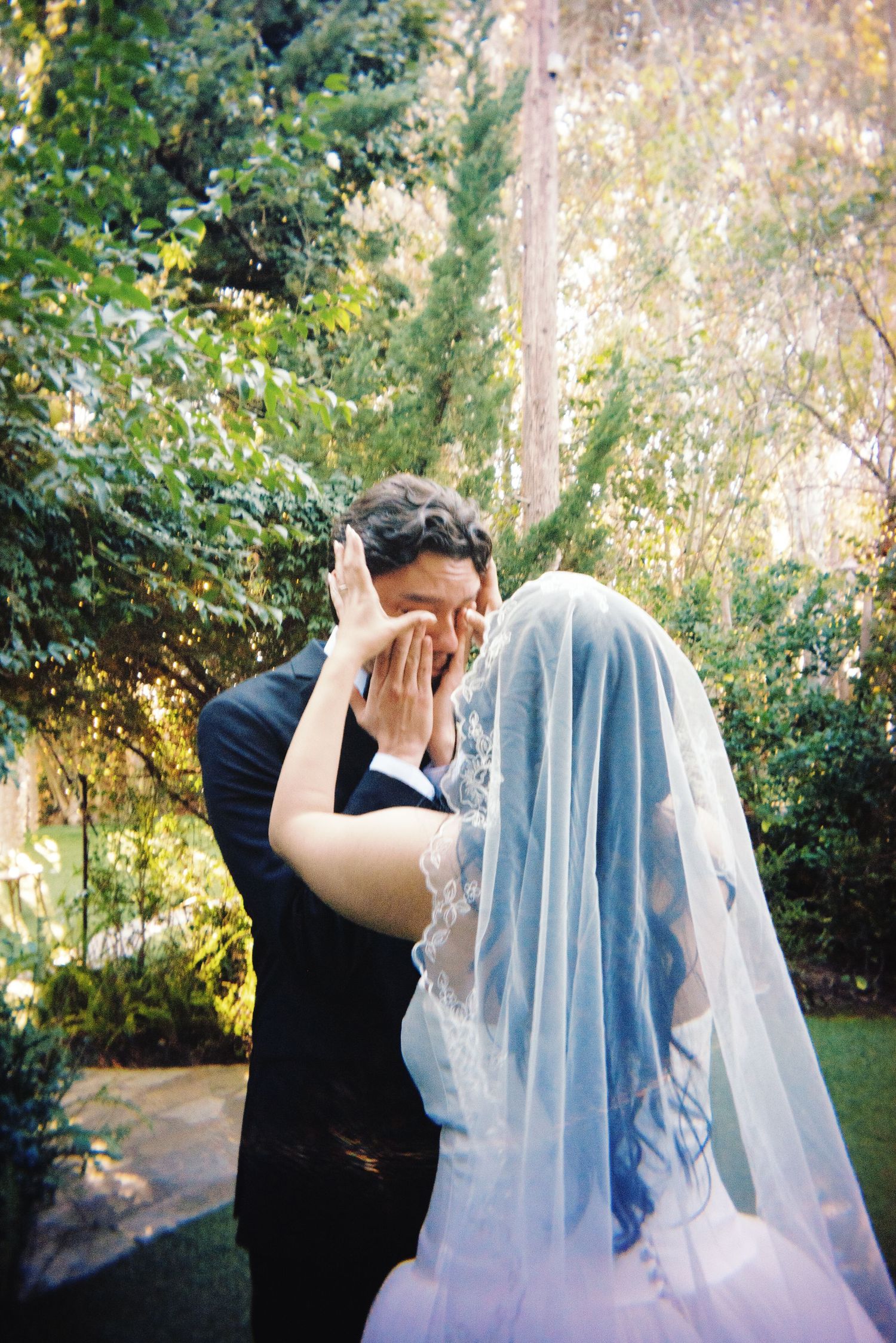 Bride and groom sharing emotional first look moment, both covering faces with hands.