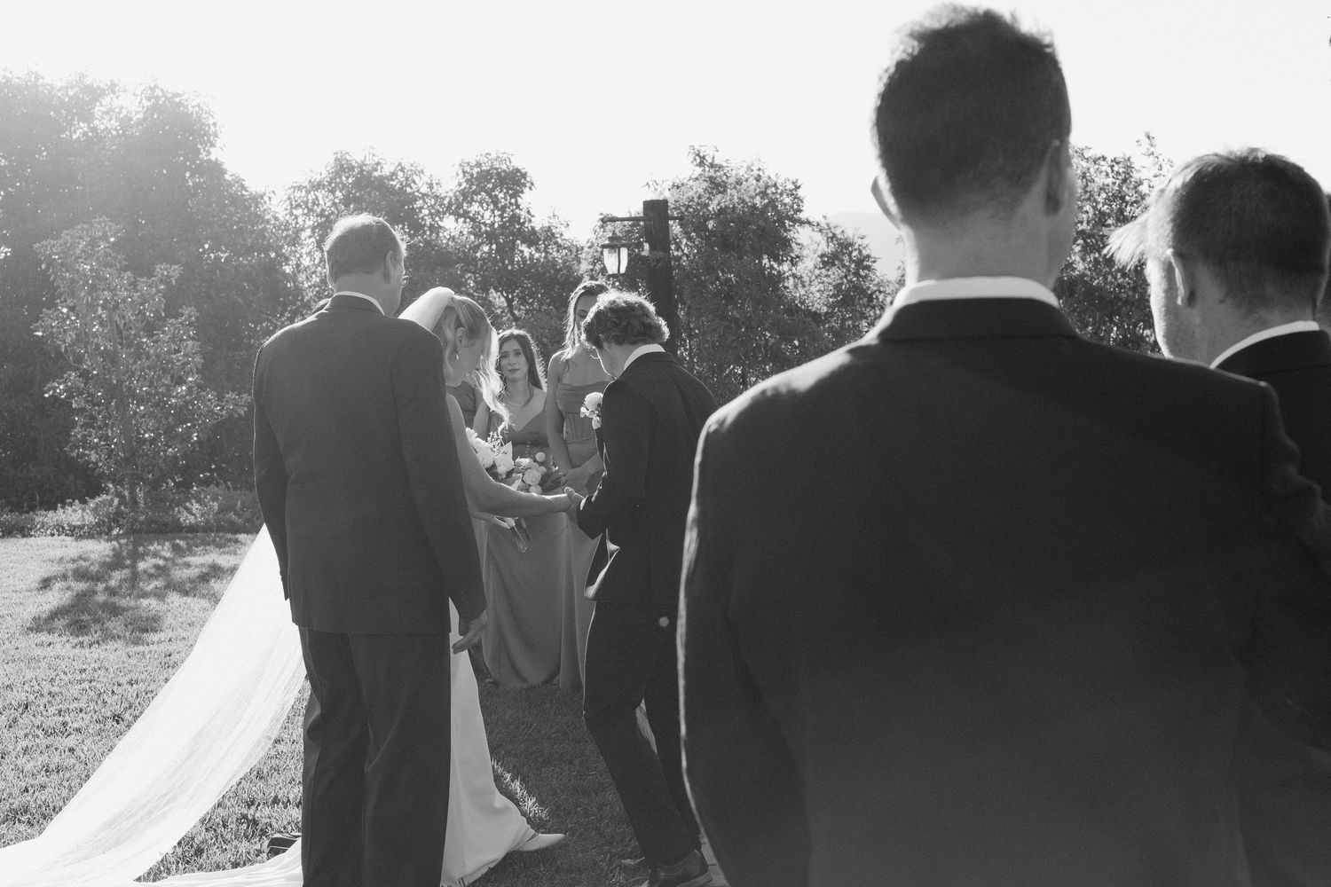 Black and white candid of groom watching bride walk down aisle at outdoor ceremony.
