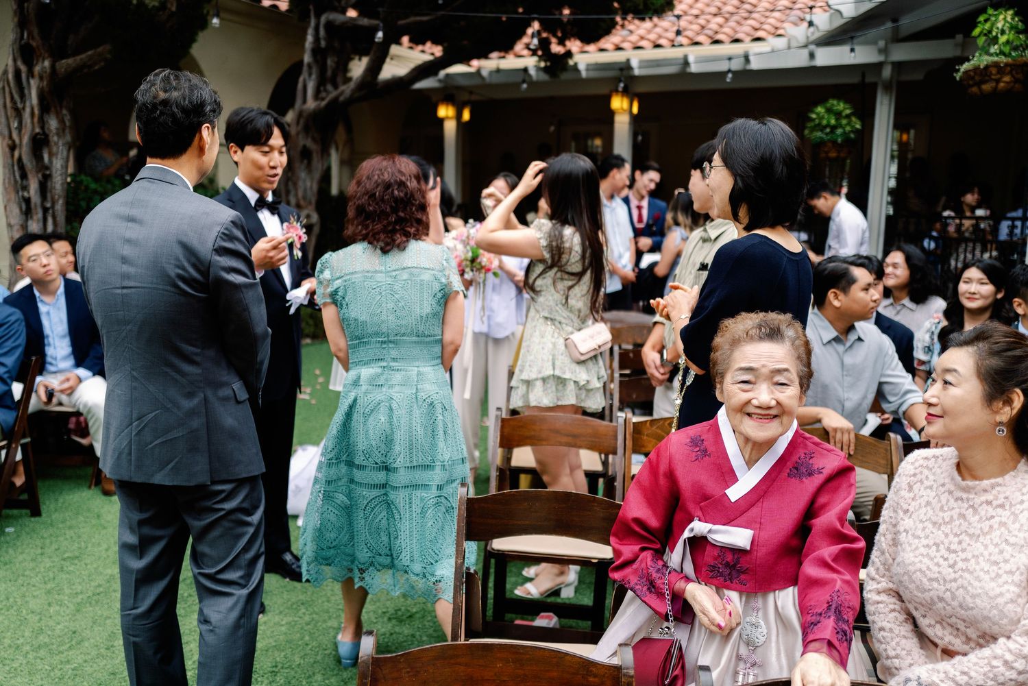 Wedding guests in traditional Korean hanbok mingle and celebrate at outdoor garden wedding reception.