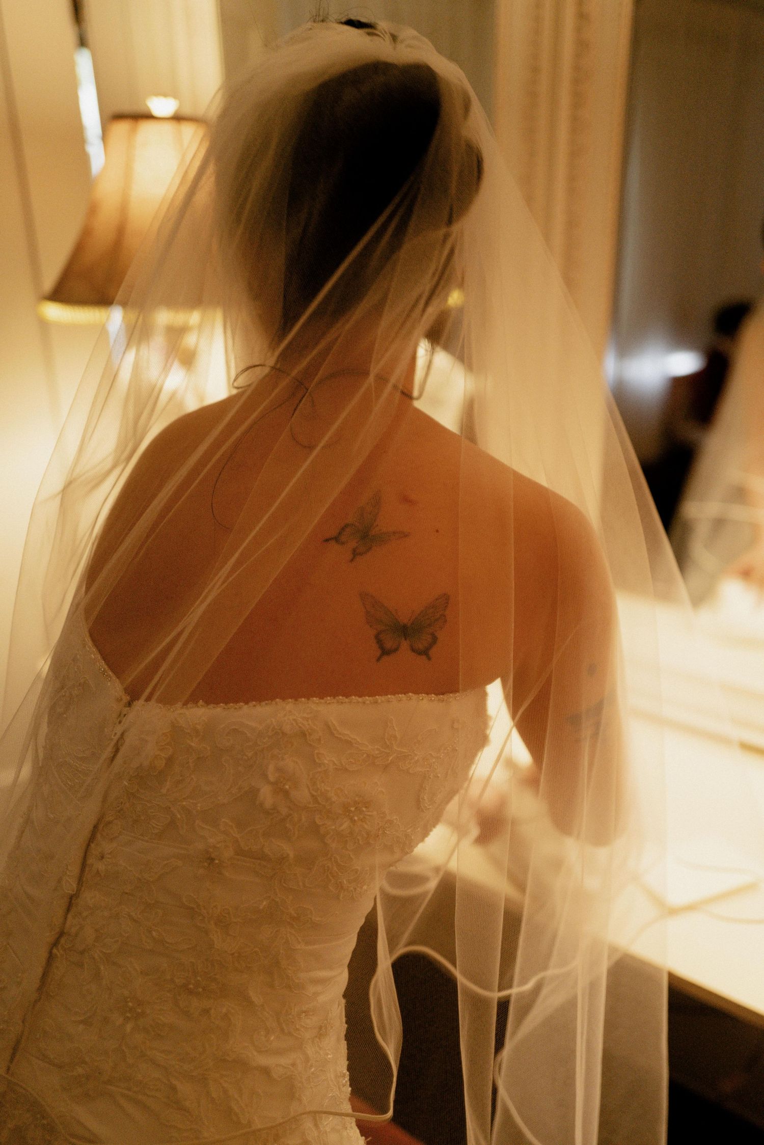 Bride in strapless lace gown with veil revealing butterfly tattoos on her upper back.