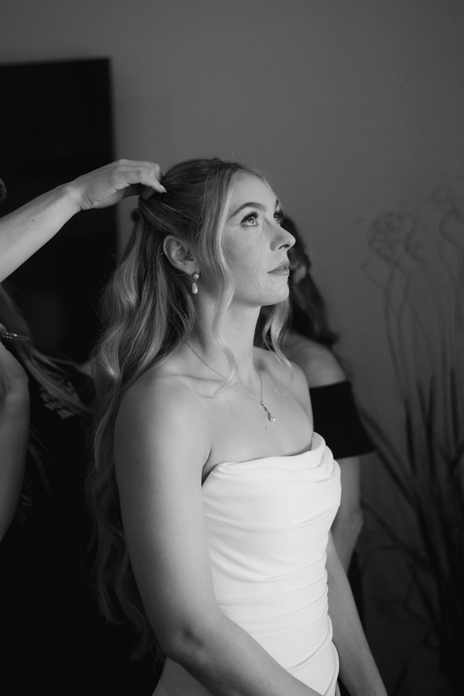 Bride in strapless white gown having hair styled, elegant black and white portrait.