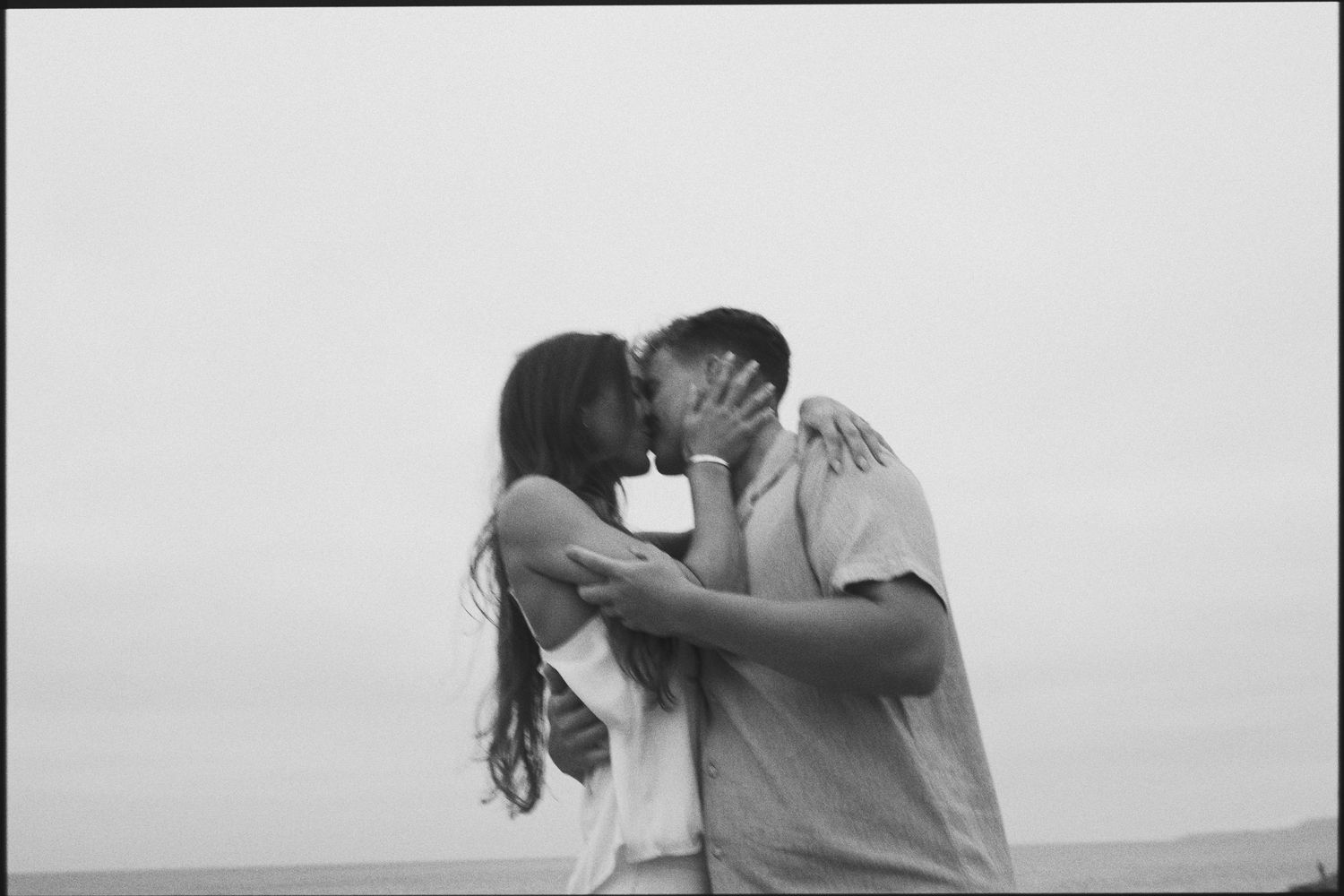 Black and white photo of a couple sharing a tender kiss on a misty beach.