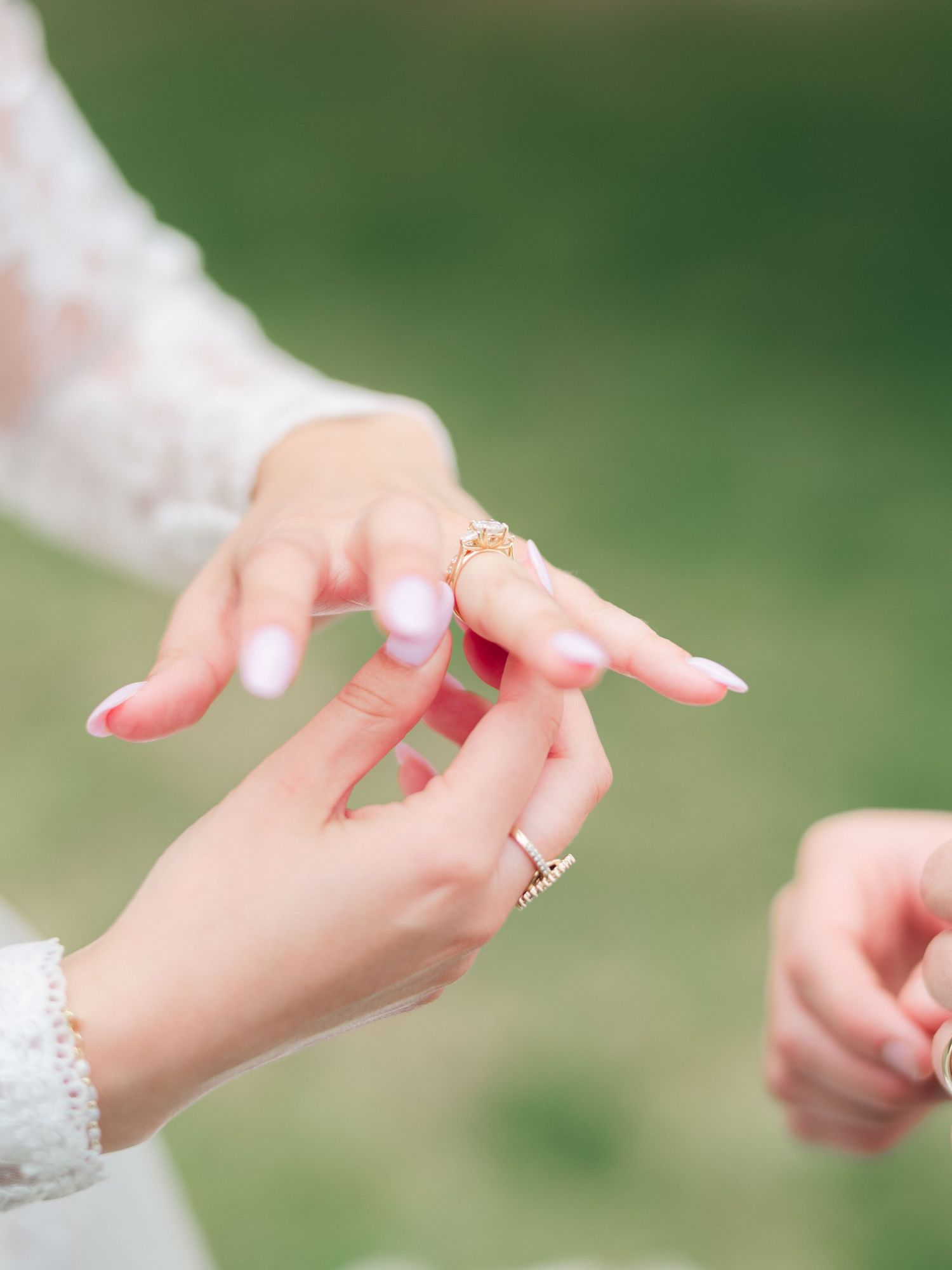 Close-up of delicate hands exchanging a gold ring during a wedding ceremony outdoors.
