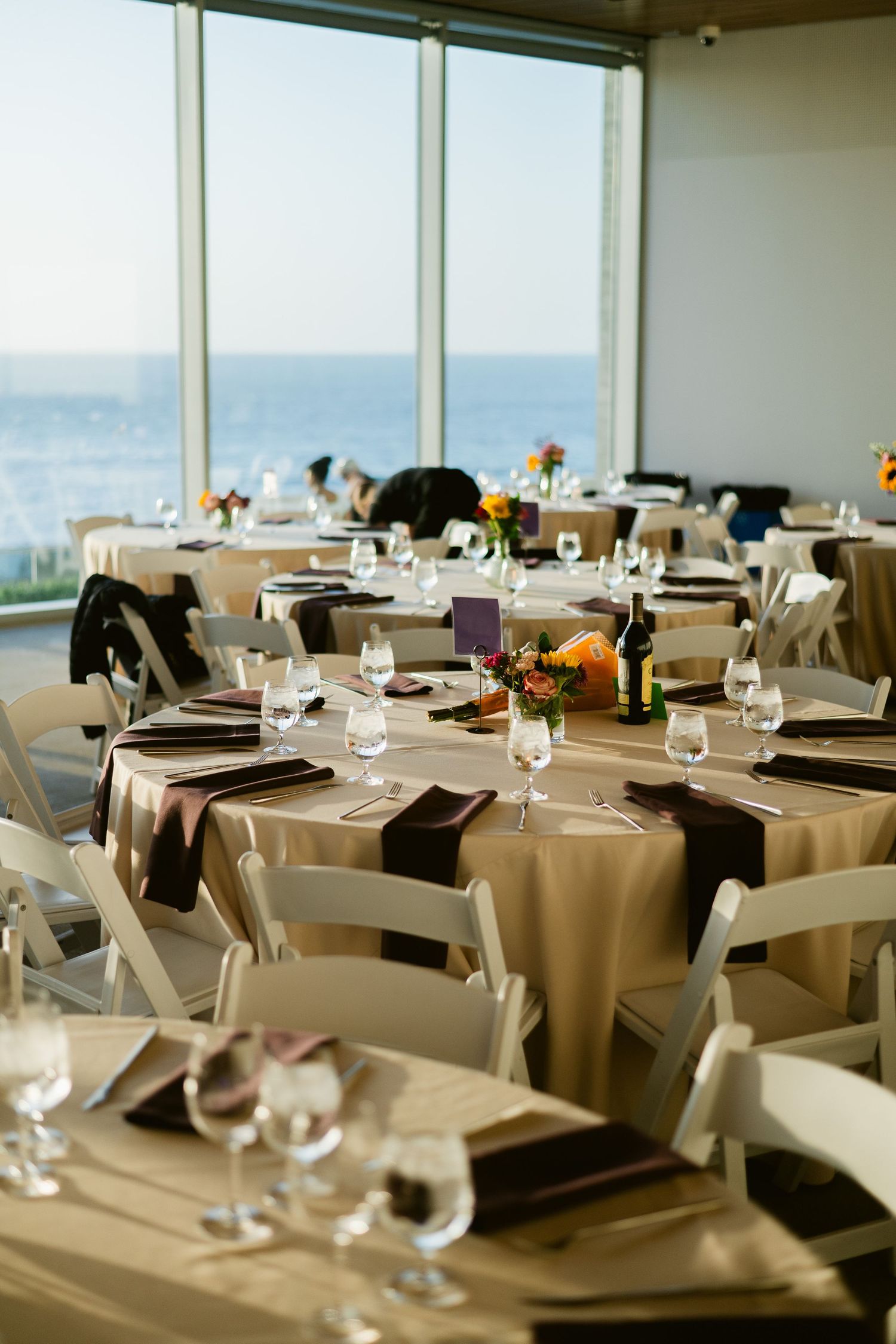 Elegant oceanview wedding reception with round tables, white chairs, champagne linens, and floral centerpieces.