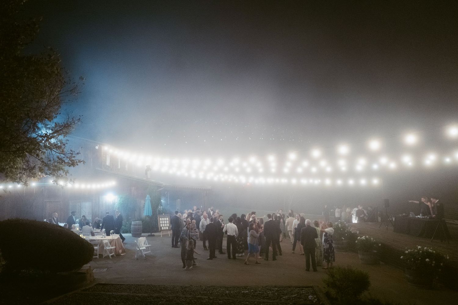 Outdoor wedding reception at night with string lights glowing through misty fog.