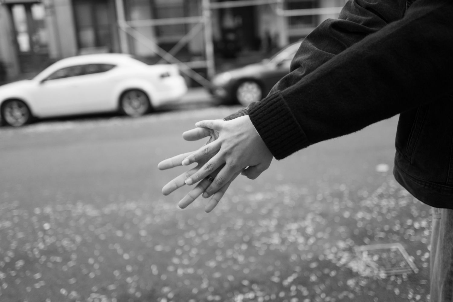 Close-up black and white photo of two people holding hands near a city street railing.
