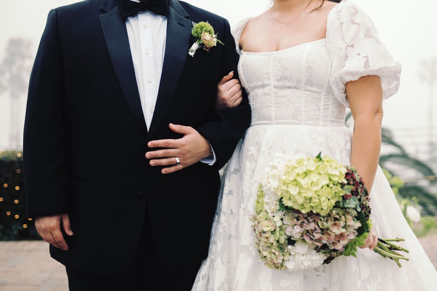 Close-up of bride holding bouquet and groom in tuxedo with boutonniere at wedding.