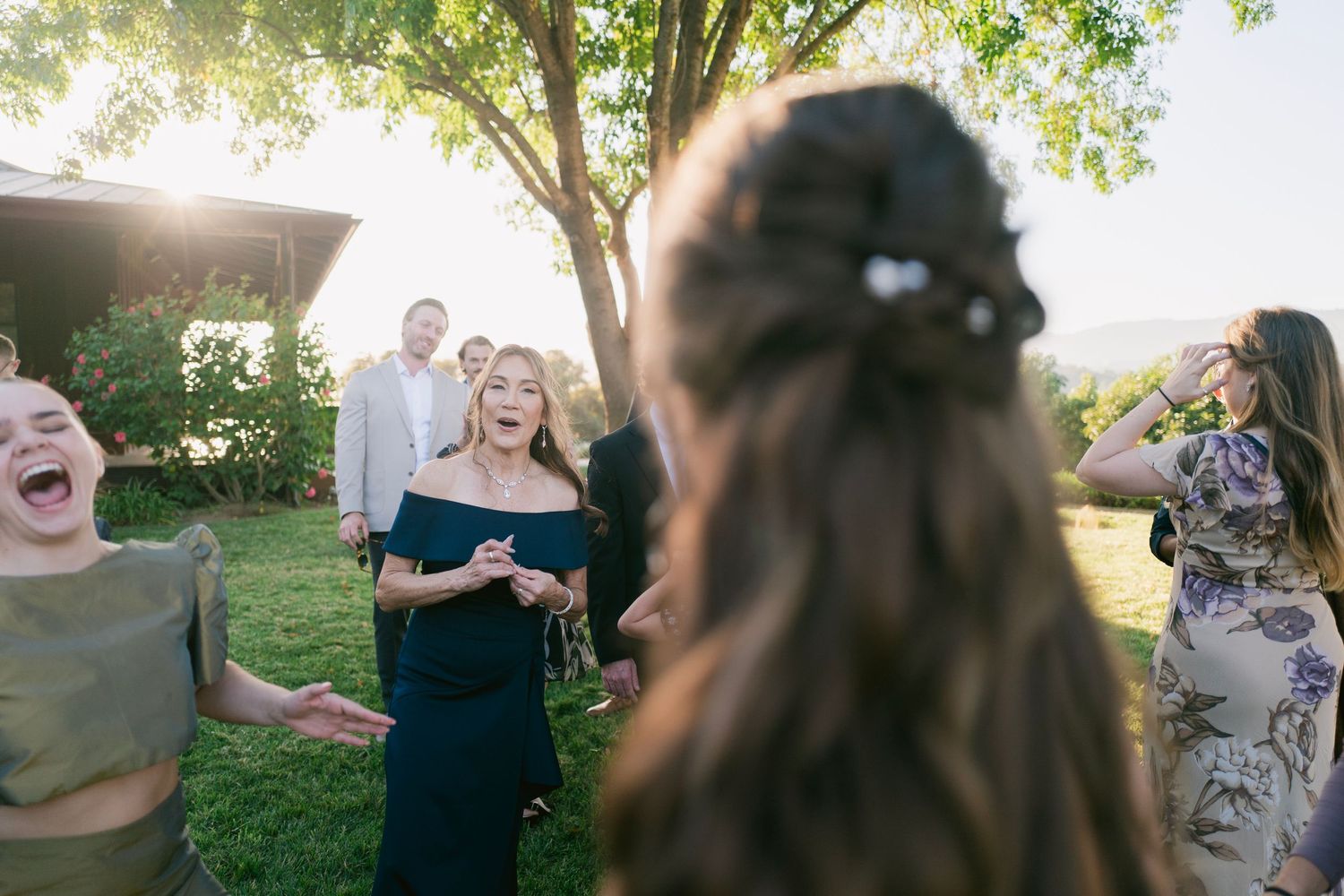 Wedding guests laughing and reacting joyfully outdoors during golden hour reception celebration.