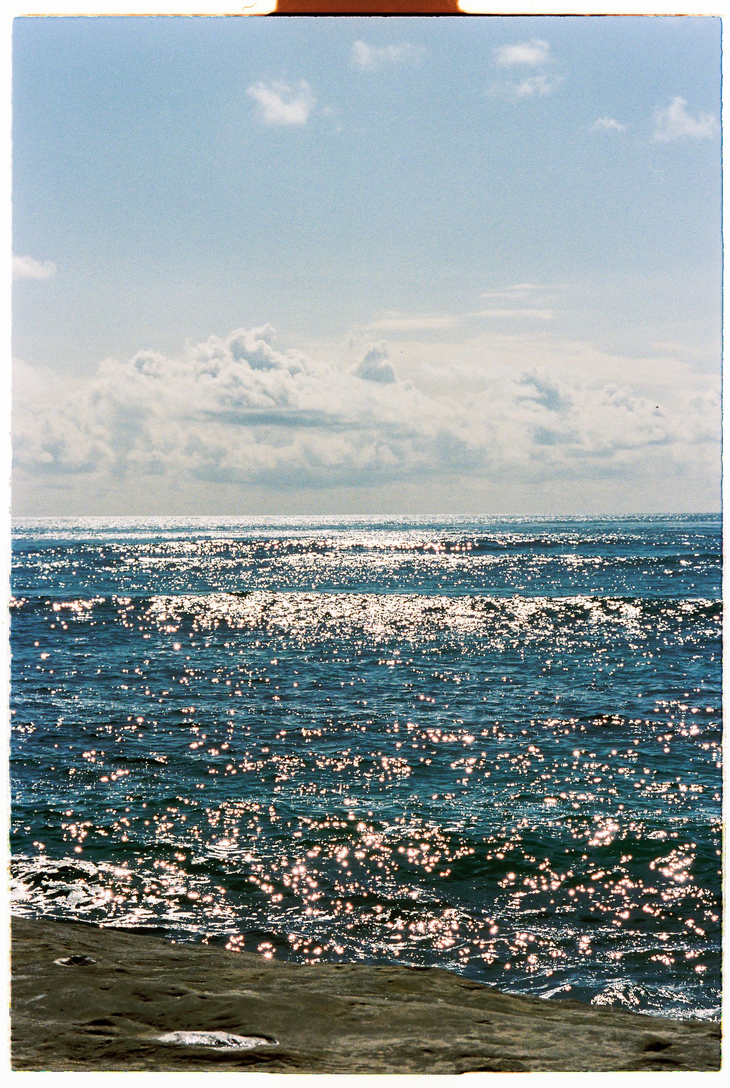 Sparkling ocean waves reflecting sunlight beneath a partly cloudy sky captured on film photography.