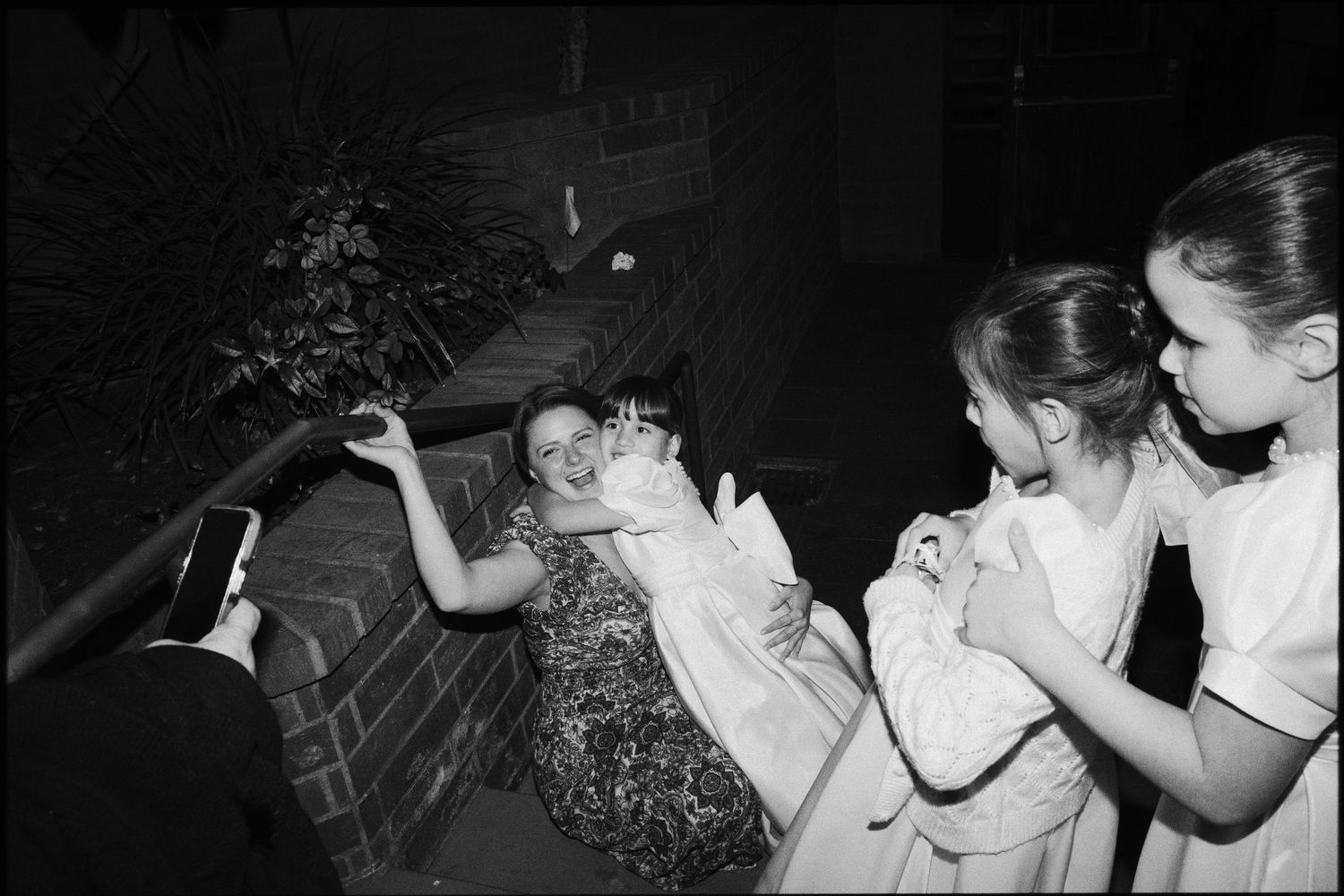 Black and white photo of young girls in formal dresses laughing on outdoor stairs at a nighttime event.