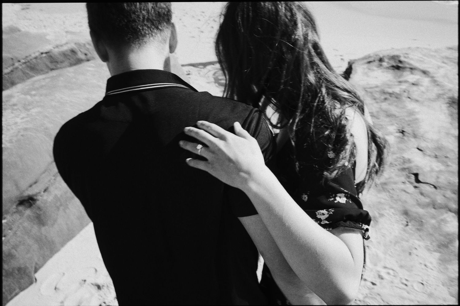 Black and white photo of woman placing hand on mans shoulder as they look out over rocky coastal landscape.