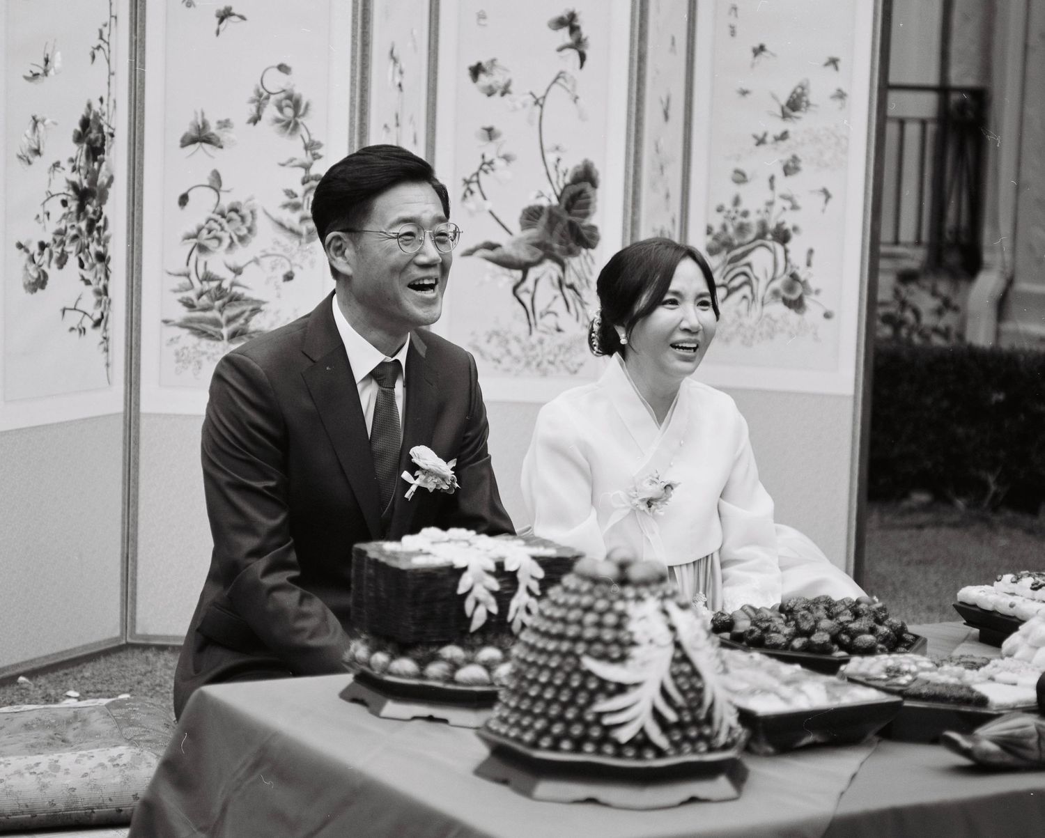 Couple laughing together at traditional Korean wedding table with ceremonial food display.