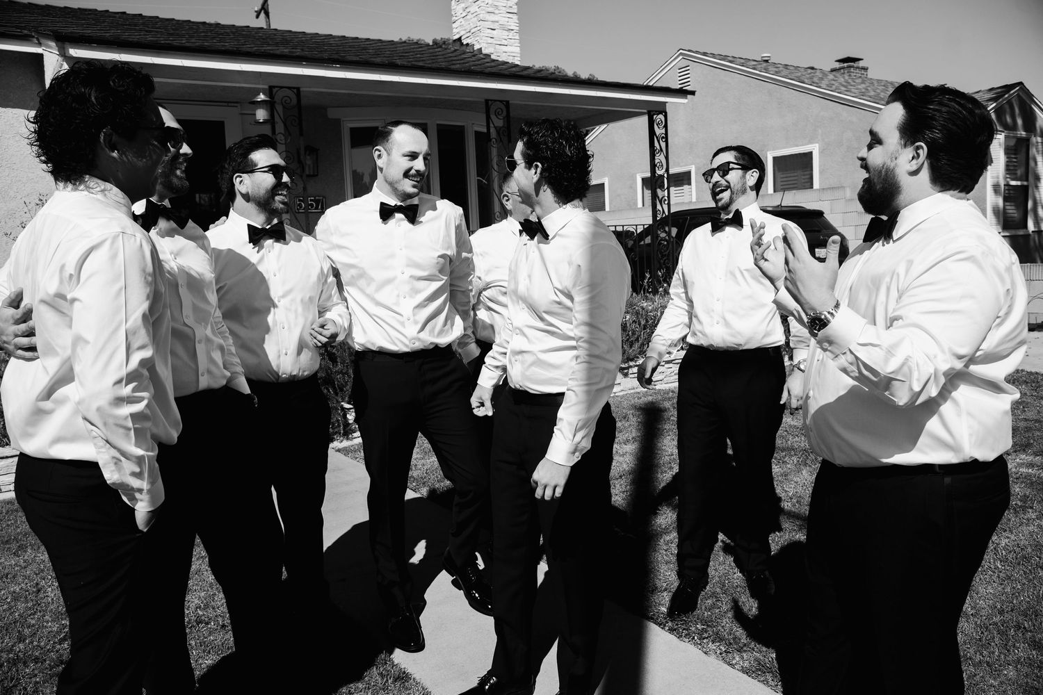 Black and white photo of groomsmen in white shirts and bow ties laughing outdoors.