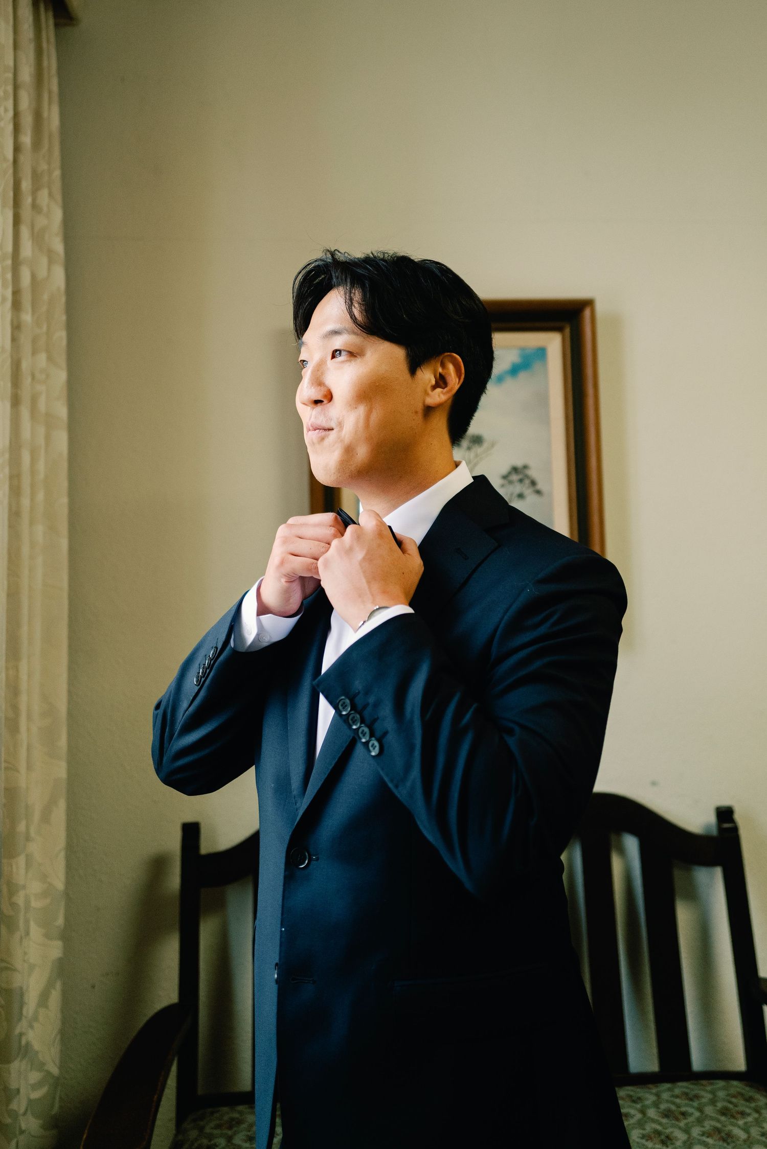 Groom in navy suit adjusting bow tie while getting ready for wedding ceremony.