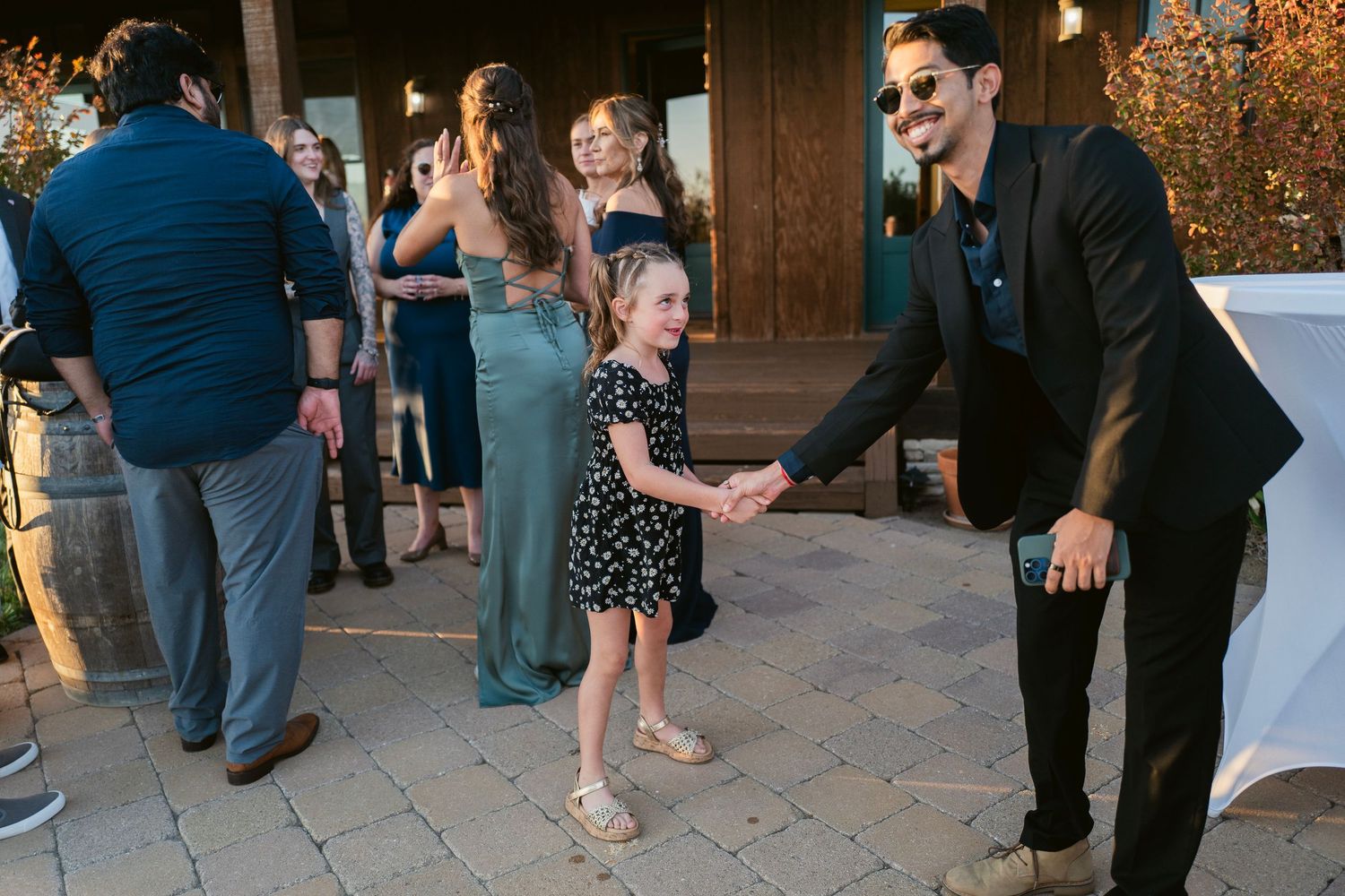 Young flower girl dances joyfully with a smiling wedding guest in a black suit at the reception.