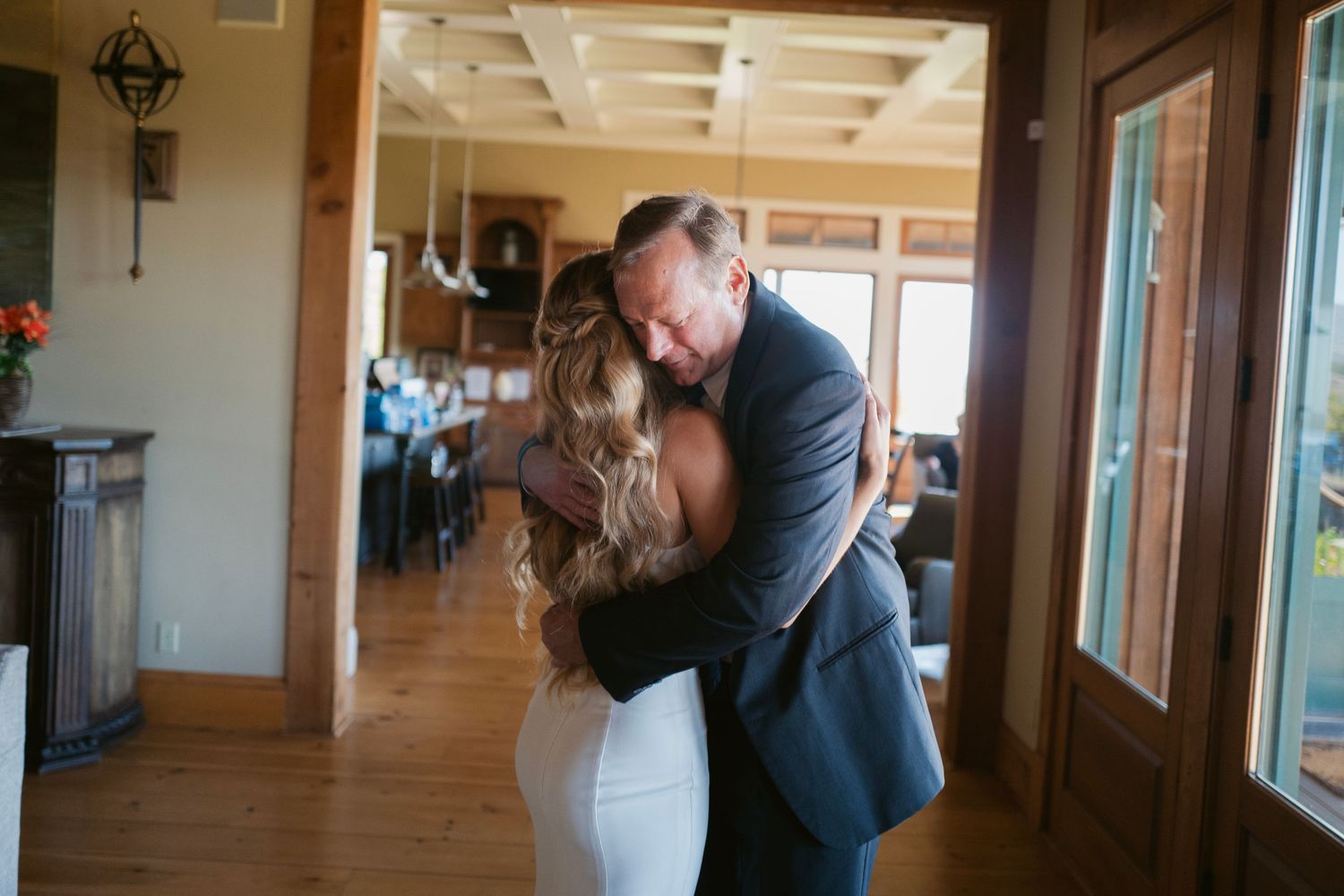 Emotional father-daughter embrace as bride in white wedding gown hugs man in blue suit.