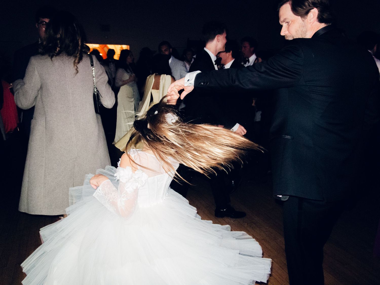 Bride in white ball gown twirls on the dance floor with a partner at a lively wedding reception.