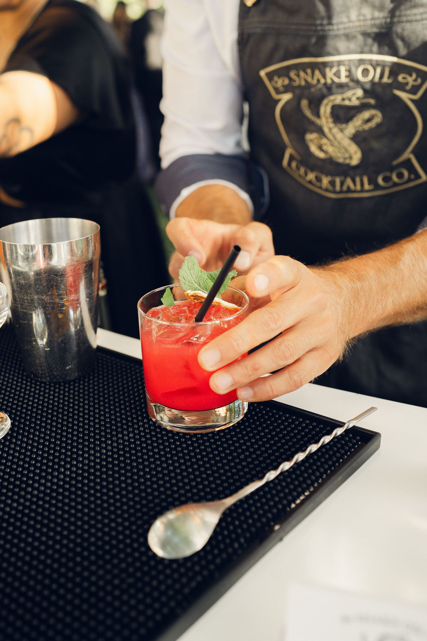 Bartender from Snake Oil Cocktail Co. garnishes a red cocktail with mint at a wedding bar.