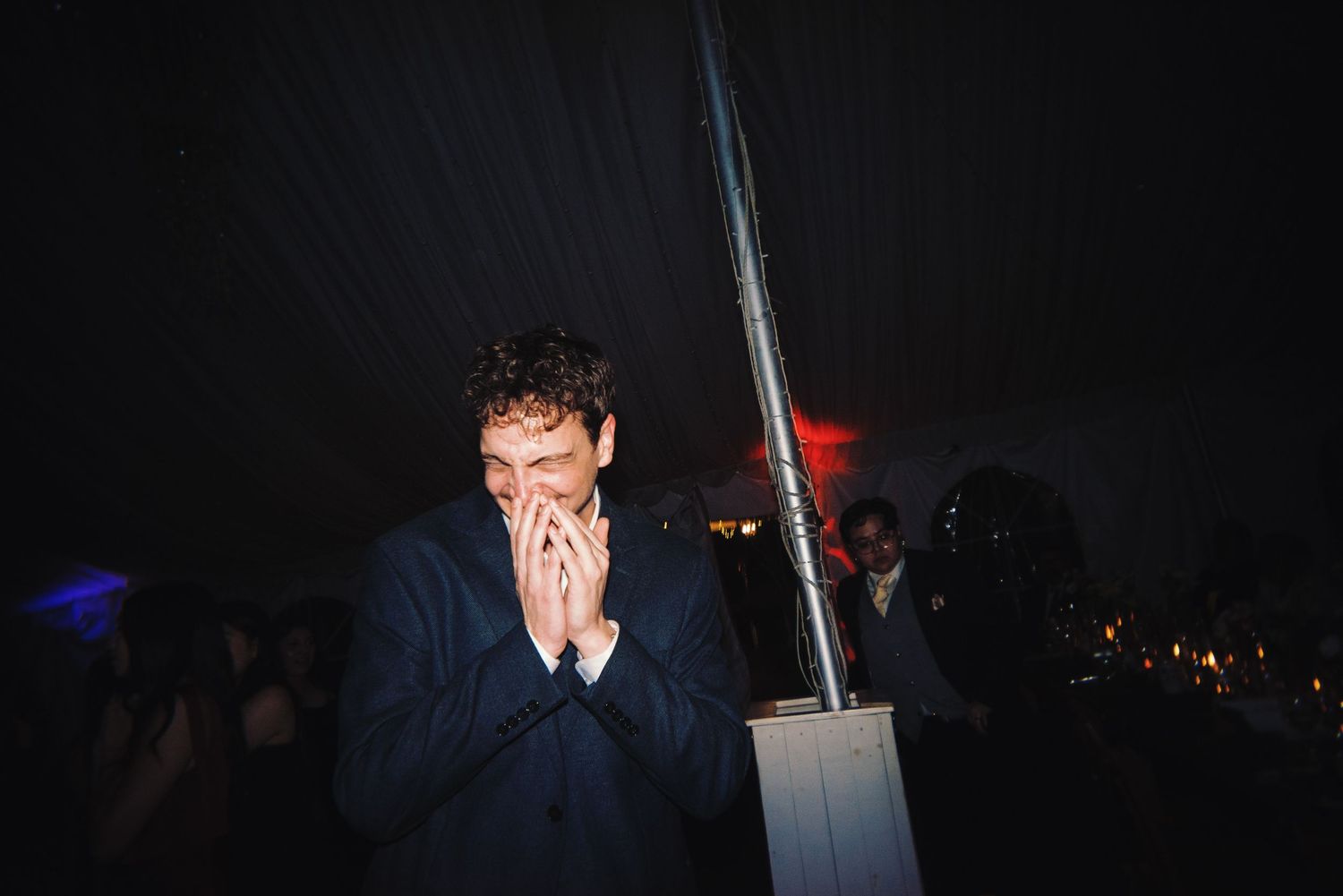 Wedding guest laughing joyfully with hands raised at lively outdoor evening wedding celebration.