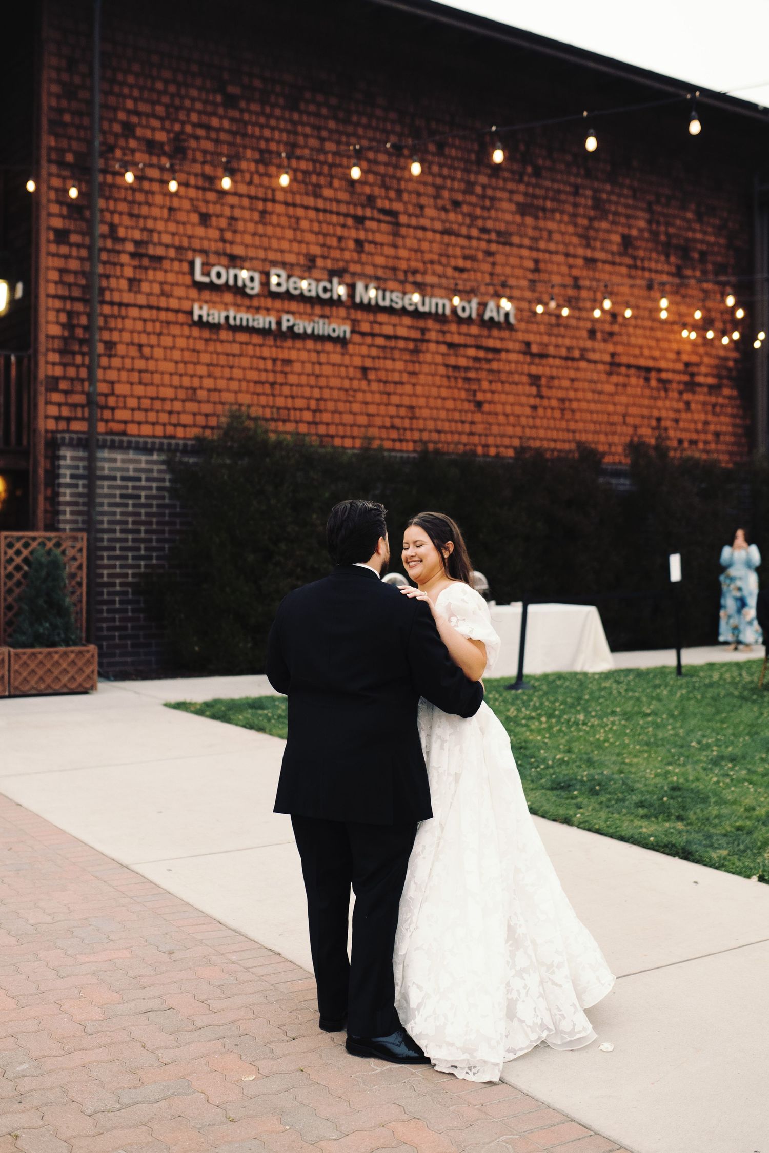 Bride and groom embrace outside the Long Beach Museum of Art Hartman Pavilion at dusk.