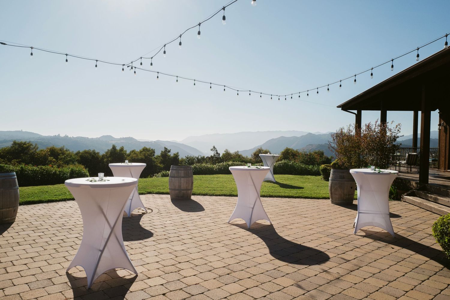 Elegant outdoor cocktail hour setup with white high-top tables, string lights, and stunning mountain views.