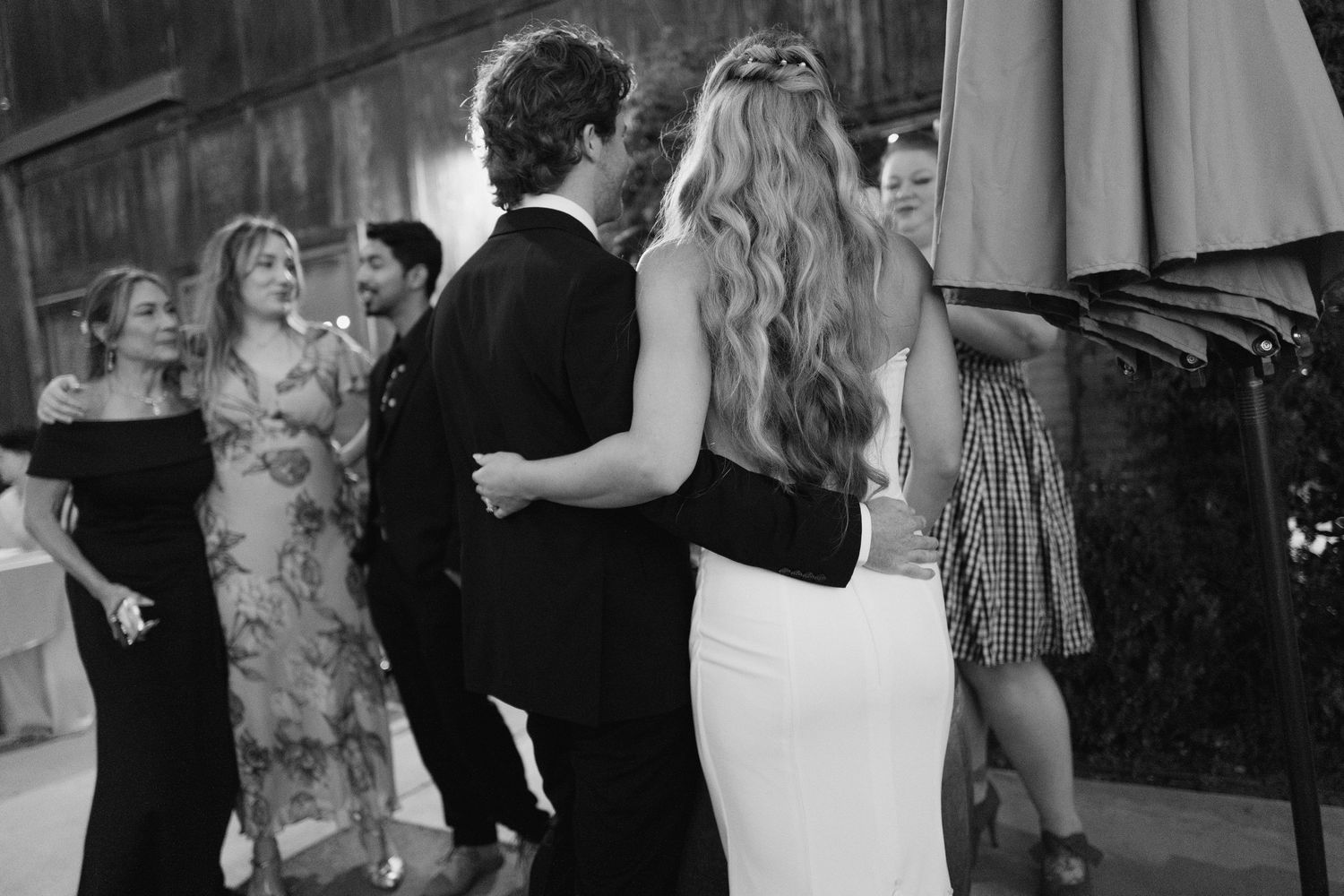 Black and white photo of wedding guests mingling and dancing outdoors at evening barn reception.