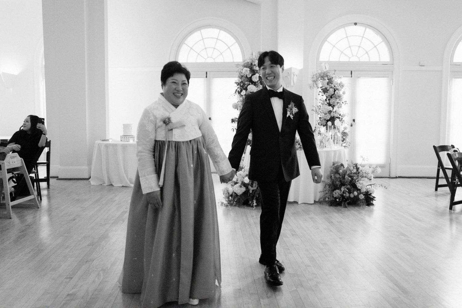 Black and white photo of groom walking with mother in hanbok at wedding.