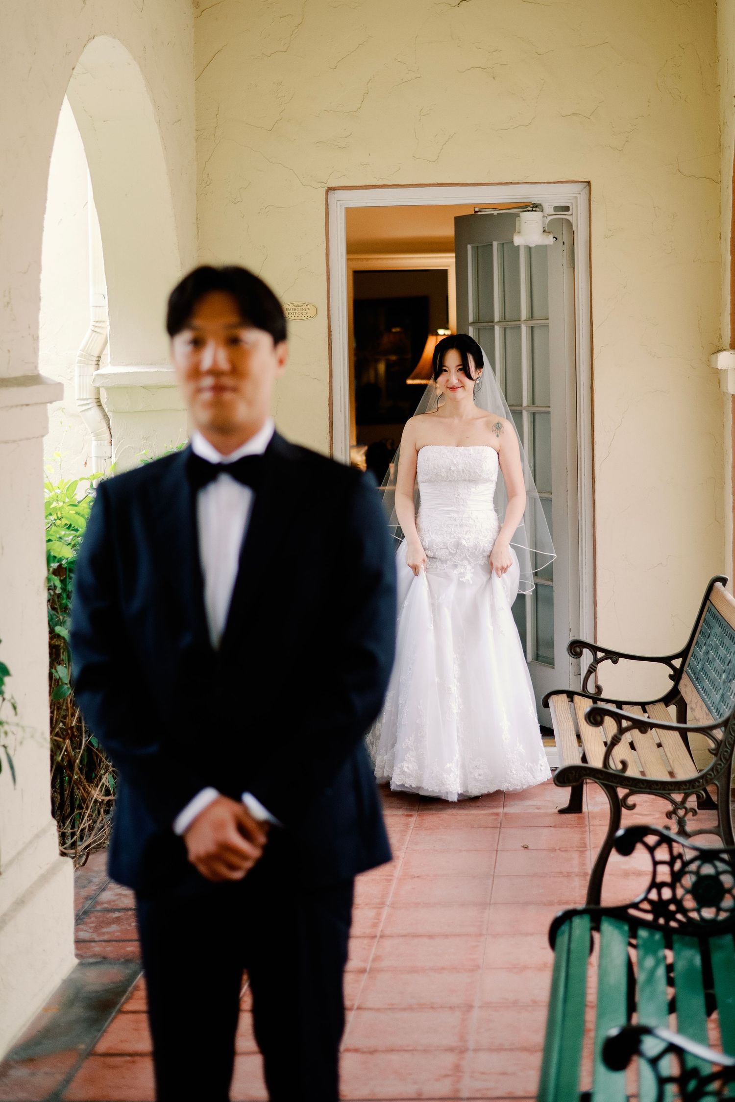 Bride in white strapless gown and veil approaching groom for first look.