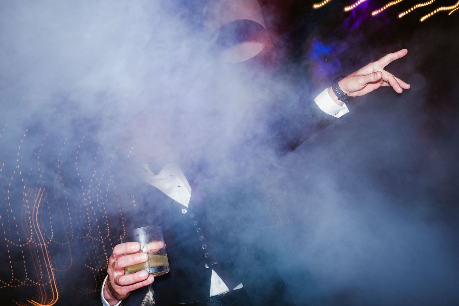 Person holding a drink in a smoky nightclub atmosphere with dramatic lighting and fog effects.