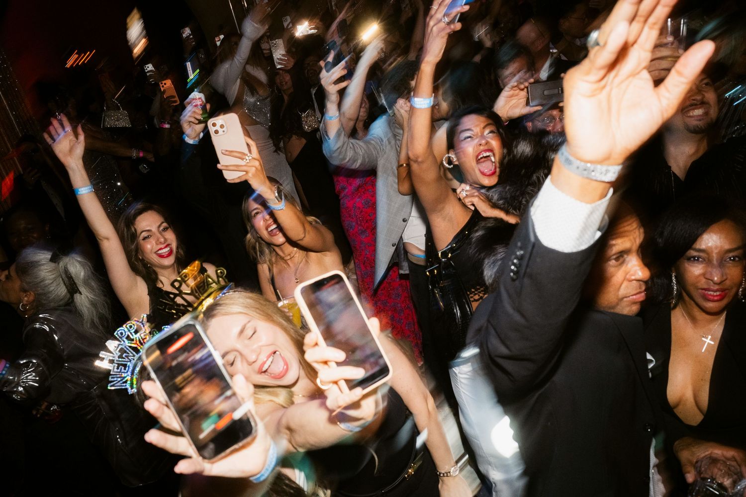 Crowd of party guests dancing and taking selfies with smartphones at a lively nightclub event.