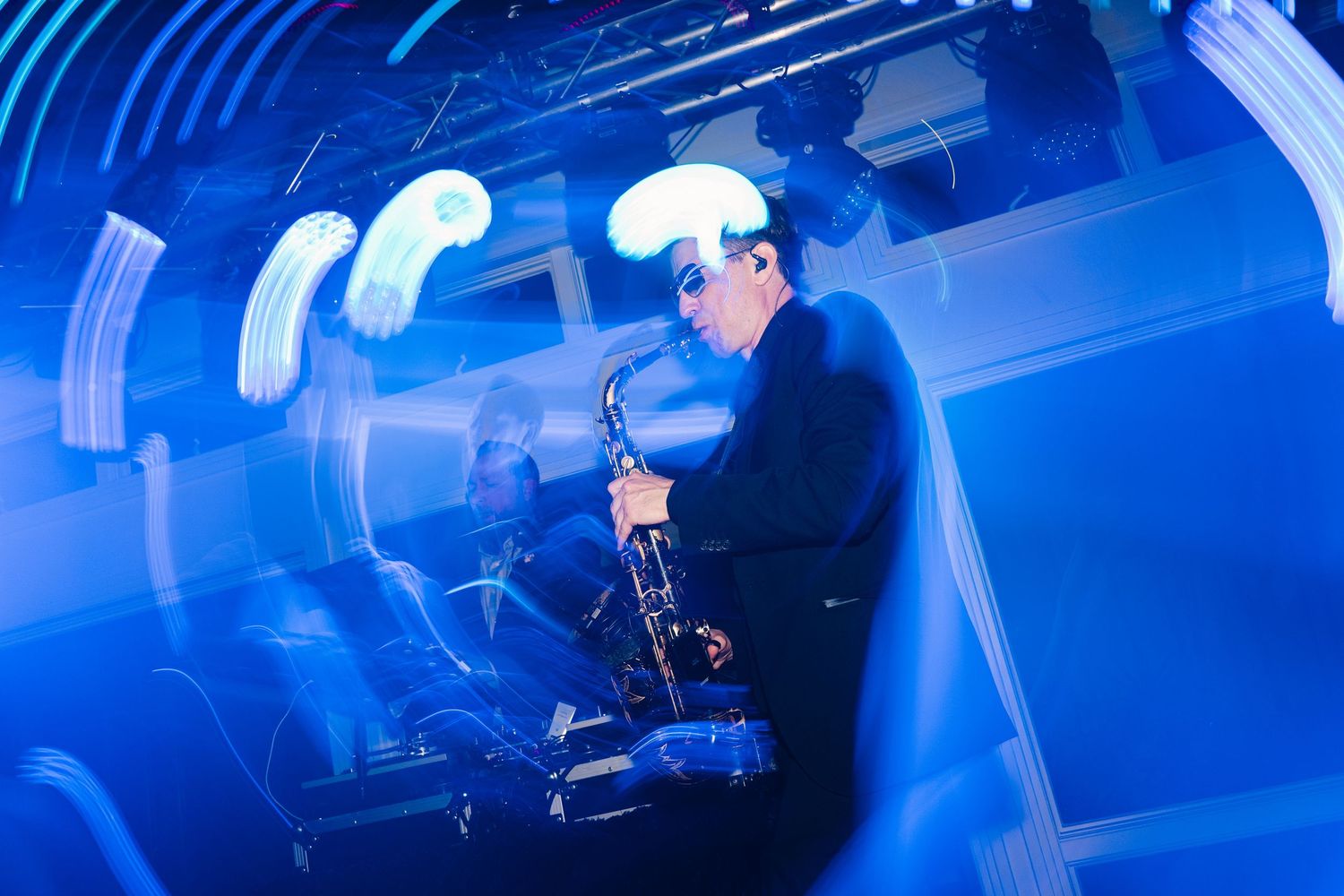Musician playing saxophone under dramatic blue stage lighting with swirling light effects in a live performance.