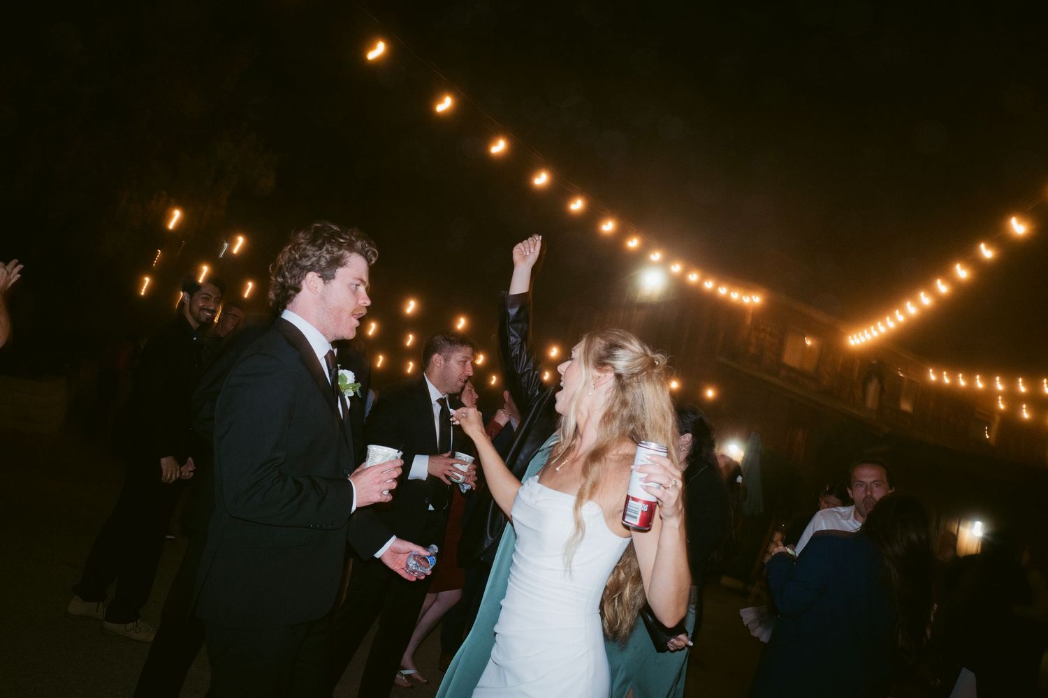 Bride and groom celebrating joyfully under string lights at their outdoor wedding reception.