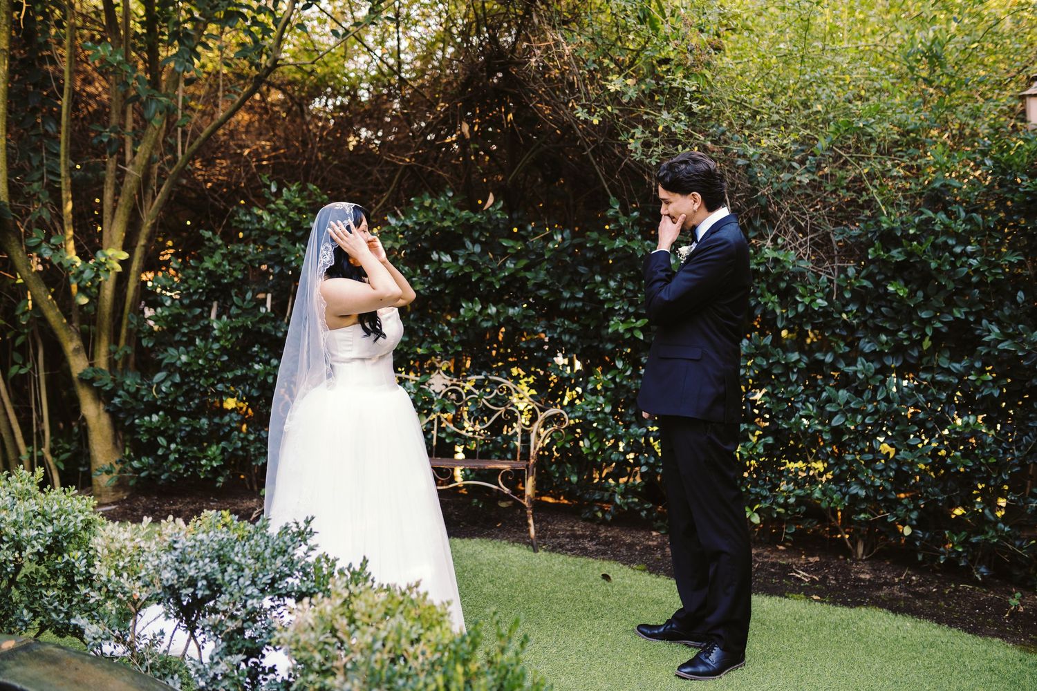 Emotional bride and groom covering faces during outdoor wedding first look moment.