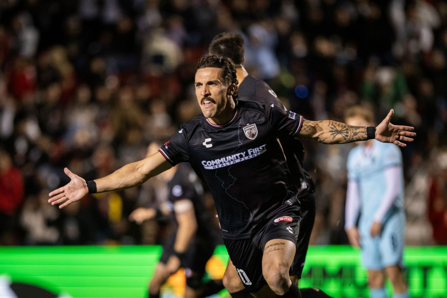 Soccer player celebrates passionately during night game under floodlights.