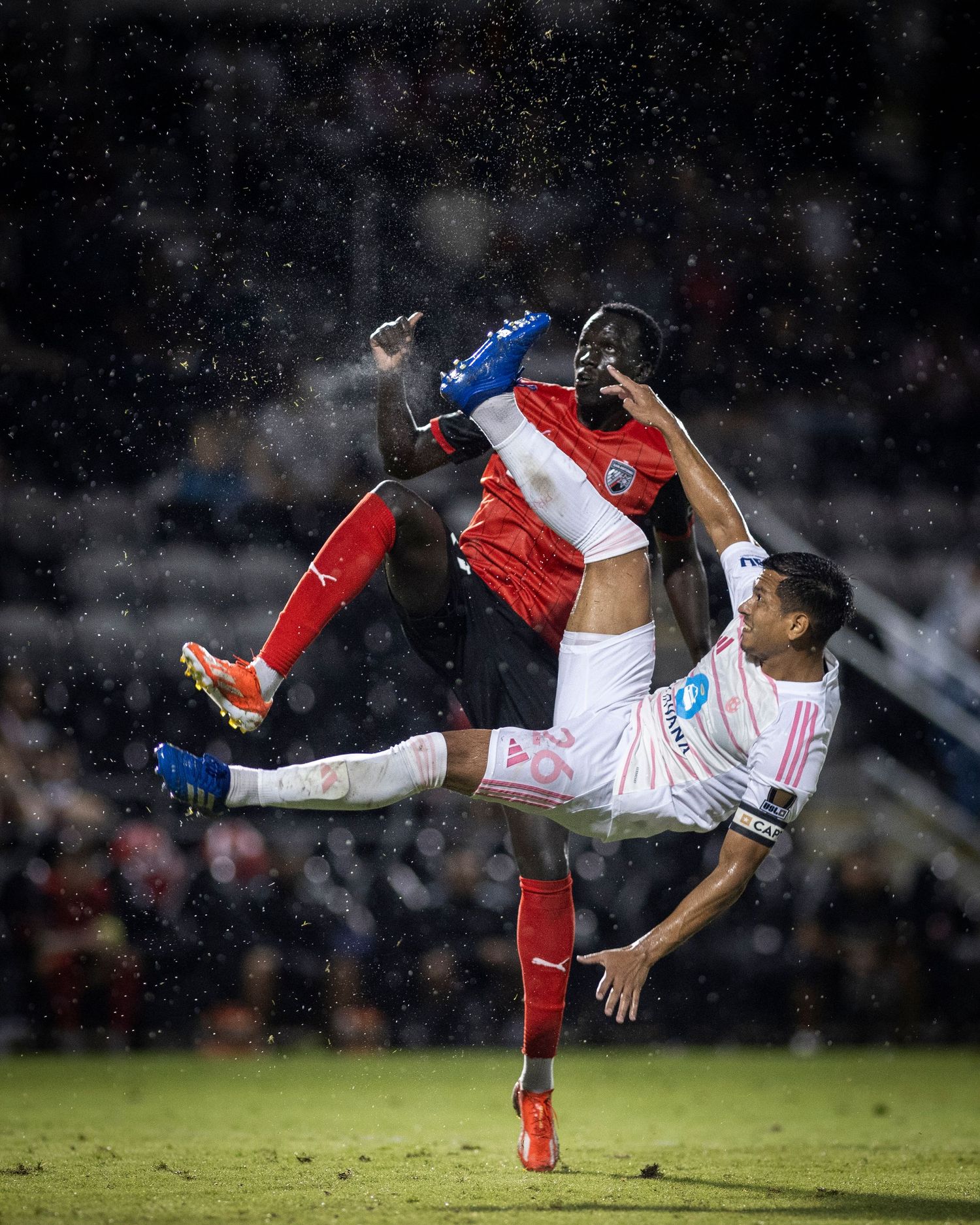 Two soccer players collide mid-air during dramatic aerial challenge in rainy conditions.