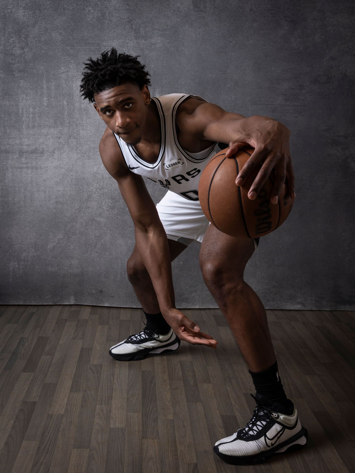 Basketball player in San Antonio Spurs uniform dribbling a ball, posing for a professional portrait photo.