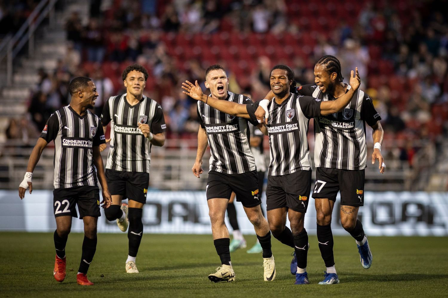 Soccer players in black and white striped jerseys celebrate together on the field.