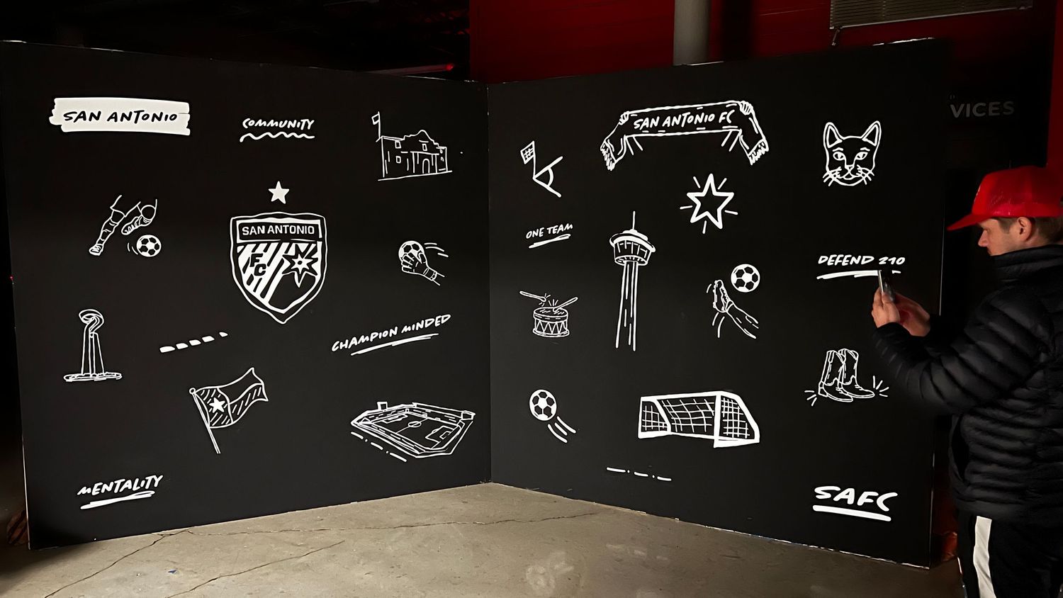 A panoramic view of a chalkboard wall covered in white hand-drawn doodles, sketches and text against a black background.