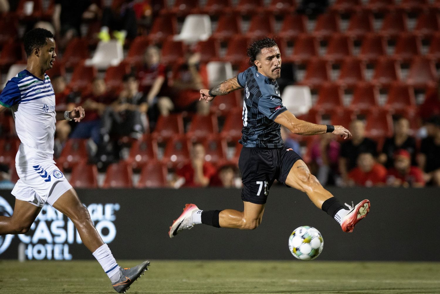 Soccer player in dark uniform volleys ball during evening match at stadium.
