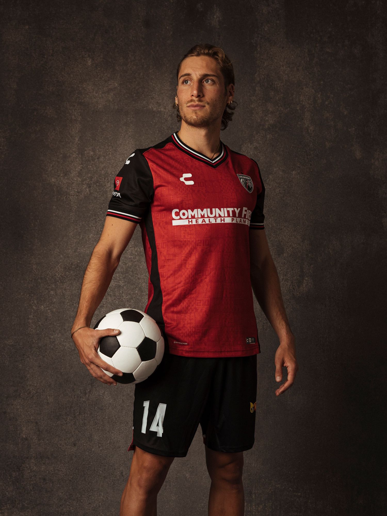 Soccer player in red number 14 jersey holding a ball, posing for a professional team portrait photo.