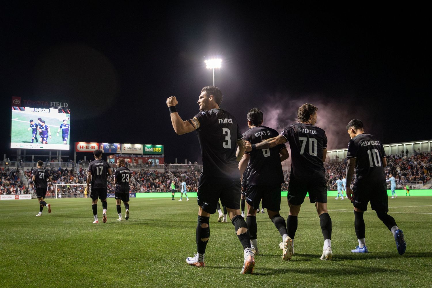 Soccer team celebrating a victory under stadium lights at night.
