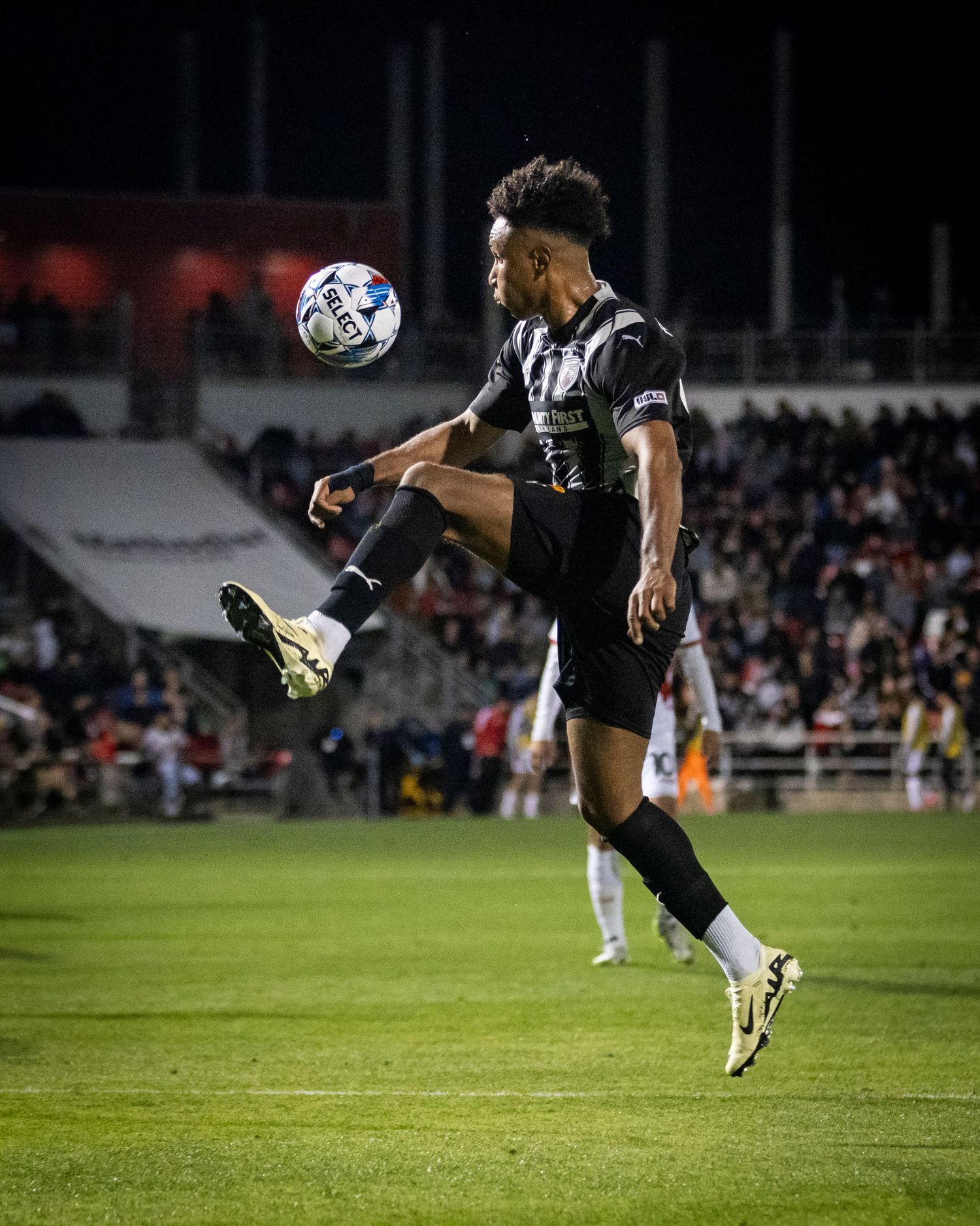 Soccer player in black uniform demonstrates ball control with high kick during match.
