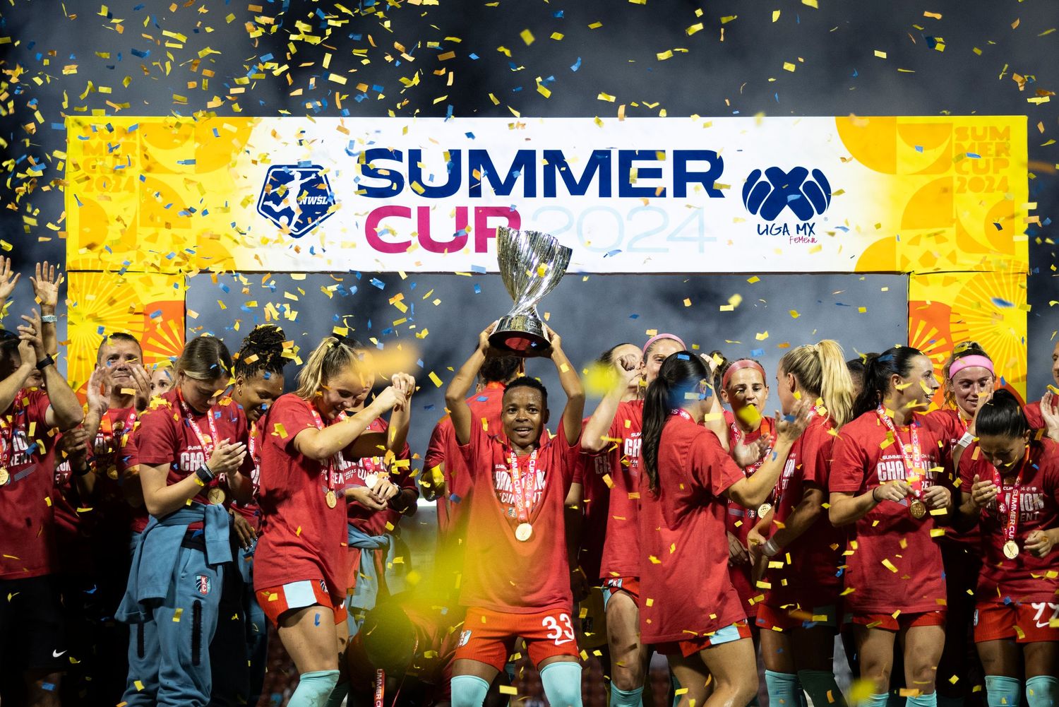 Team celebrates Summer Cup victory with trophy and yellow confetti falling under bright stadium lights.