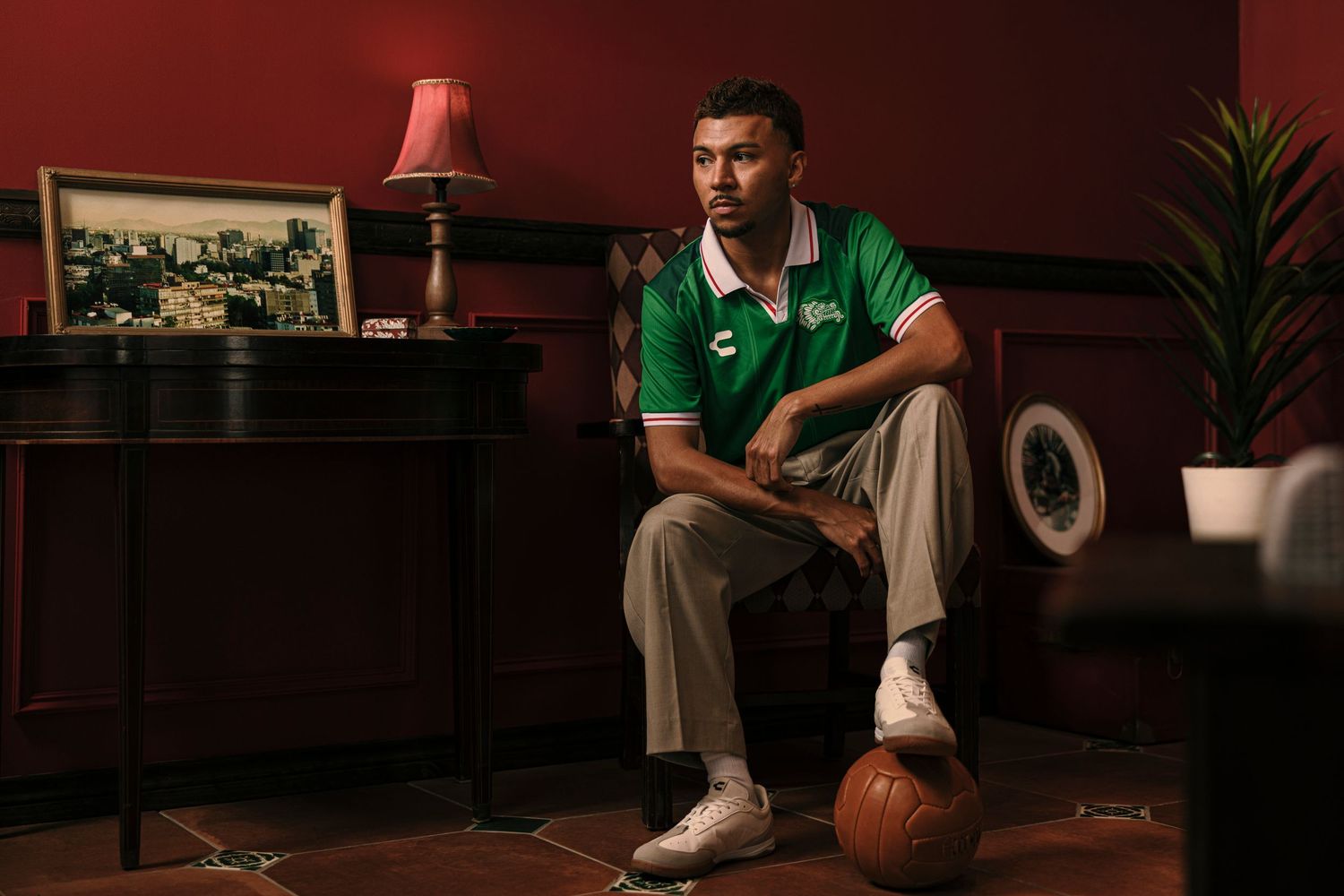 Person in green shirt sits on dark couch with basketball while watching TV in dimly lit living room.