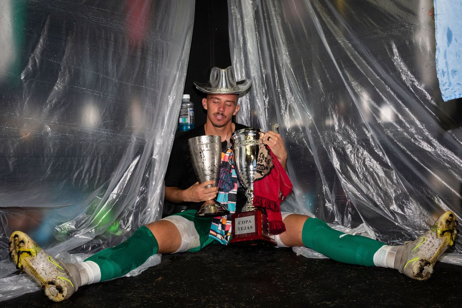 Player sits on floor with trophies while wearing cowboy hat and green socks.