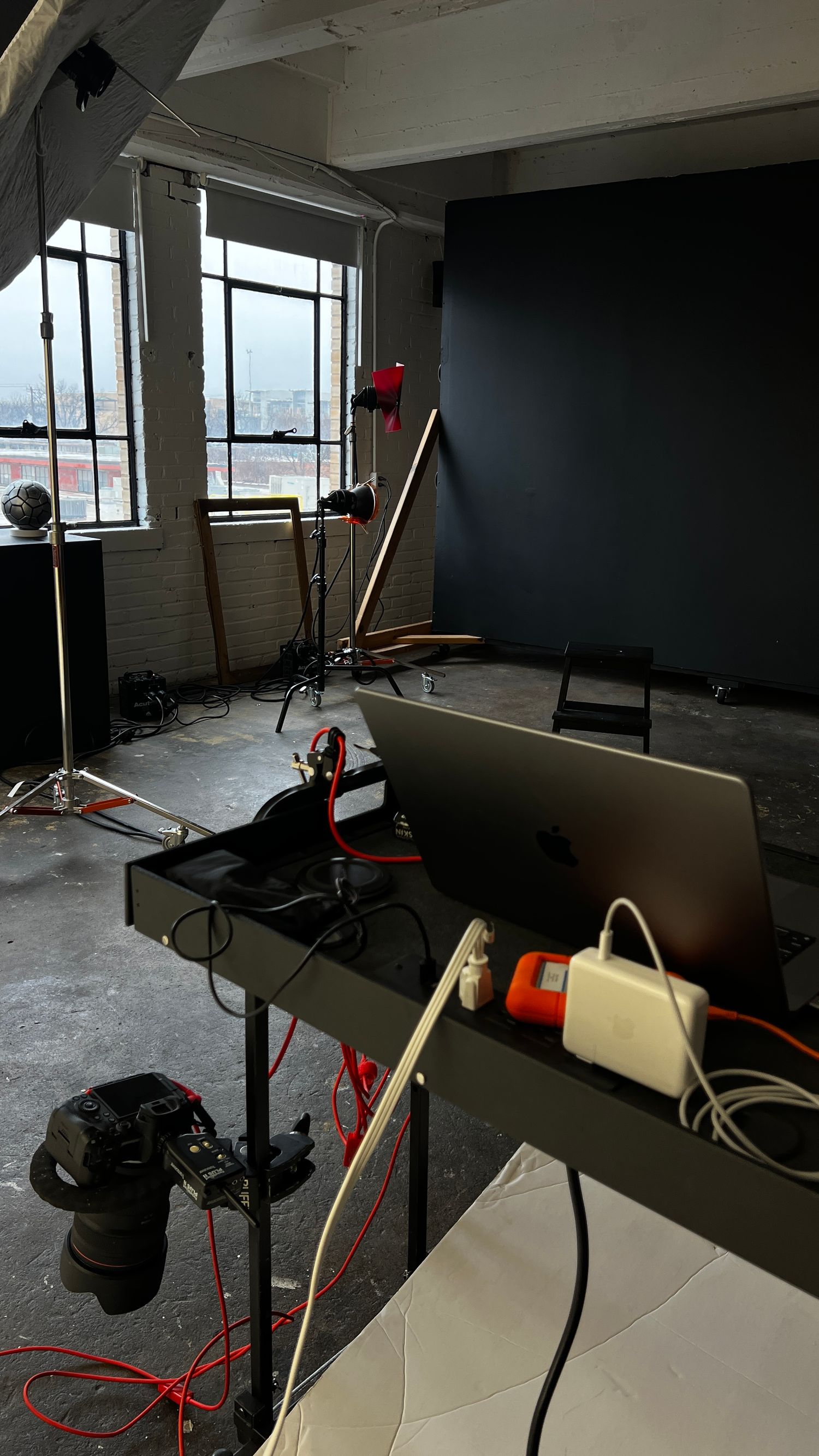 Dark studio workspace with computer setup, camera equipment and window view of city skyline in background.