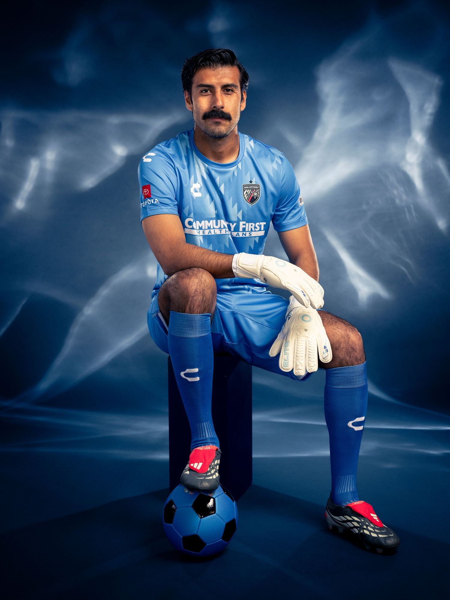 Soccer goalkeeper in blue uniform kneeling with ball, wearing gloves, Community First jersey sponsor.