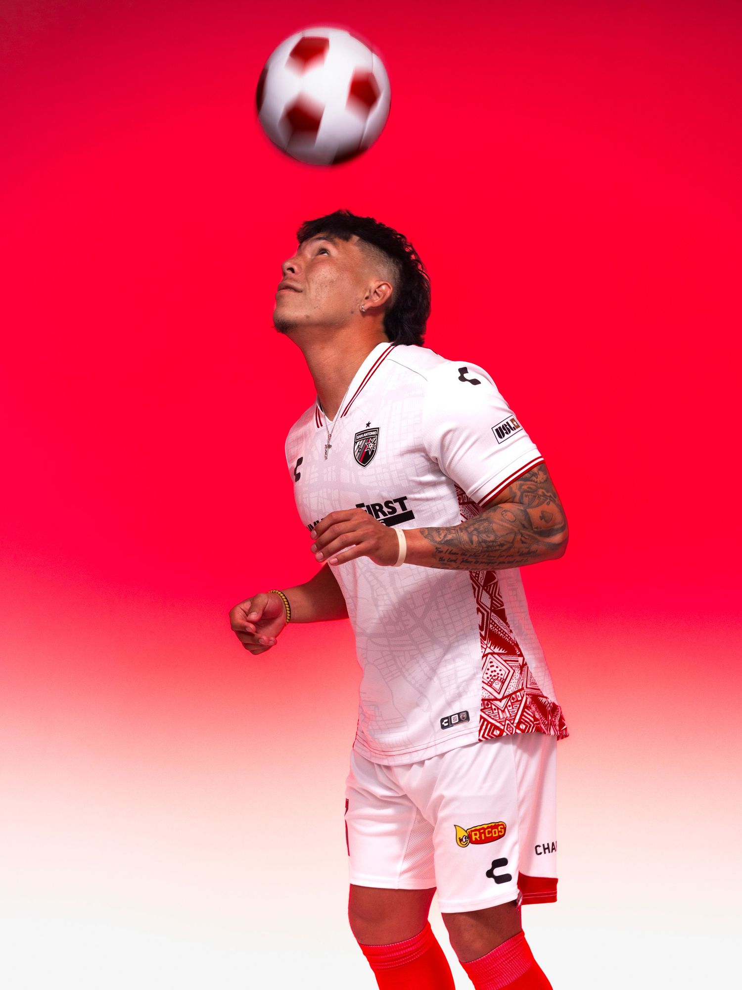 Soccer player in white Chupacabras jersey heading a ball against a red gradient background.